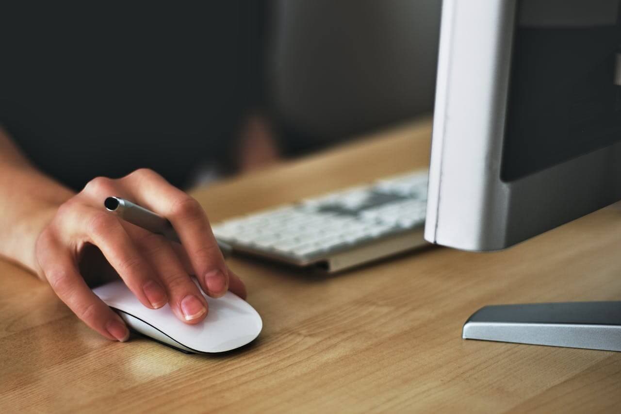 Eine Person verwendet eine Computermaus an einem Schreibtisch. Auf dem Computermonitor wird eine Klickkarte angezeigt, im Hintergrund die Tastatur.