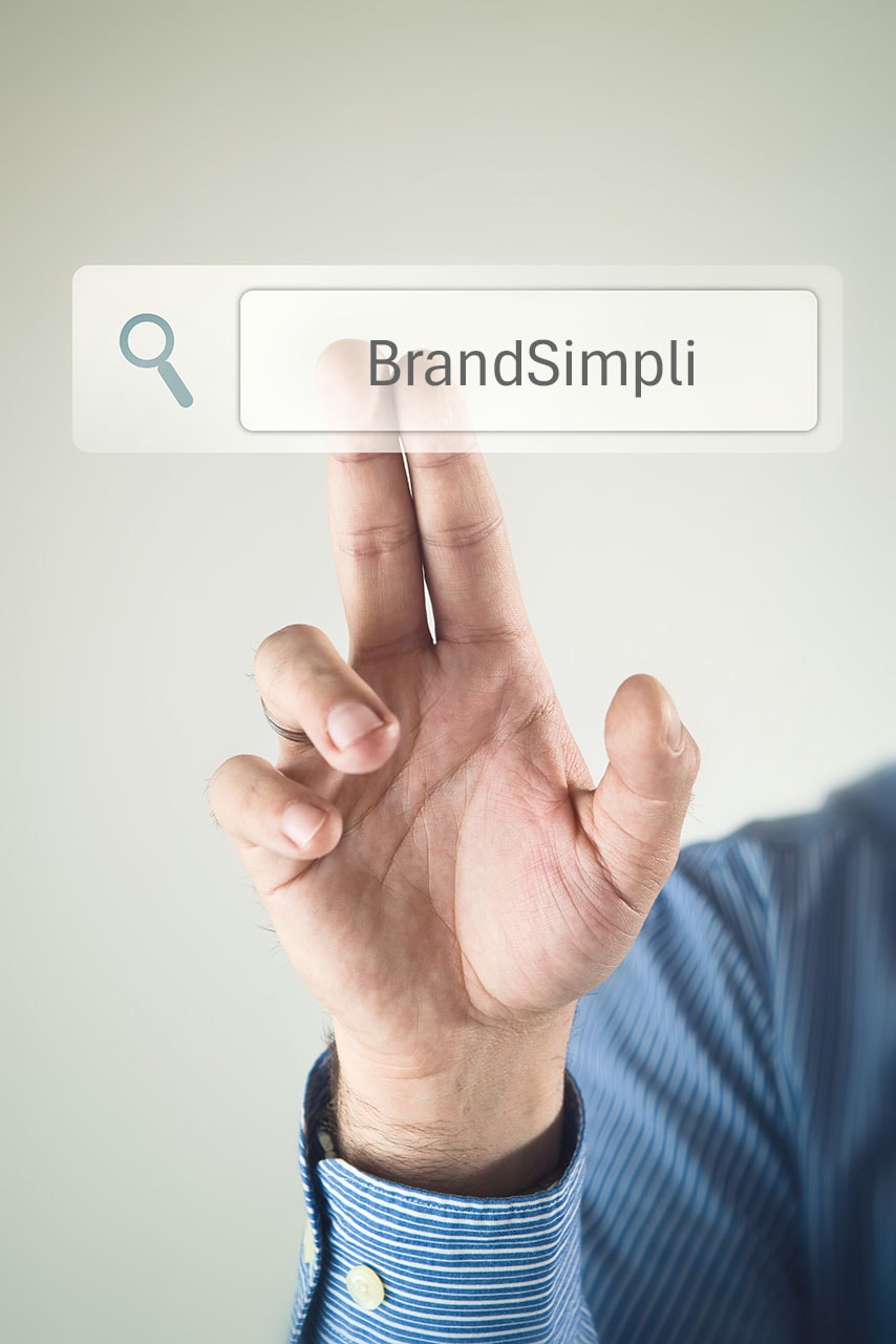 Eine Person in einem blau gestreiften Hemd drückt mit dem Zeigefinger auf eine virtuelle Suchleiste, die das Wort "BrandSimpli" mit einem Lupensymbol anzeigt und verdeutlicht, wie sich Native Ads nahtlos in digitale Erlebnisse integrieren lassen.