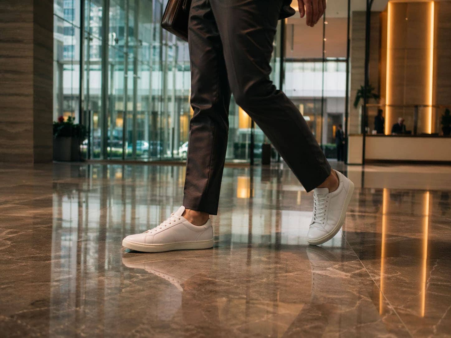 Nahaufnahme eines Mannes in schwarzen Anzughosen und weißen Sneakers im modernen Bürogebäude.