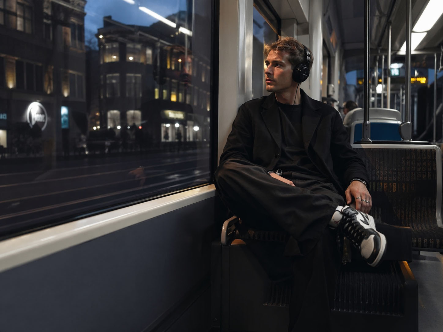 Junge Frau mit Kopfhörern, die im Bus unterwegs ist, bei Nacht, urbanes Umfeld.