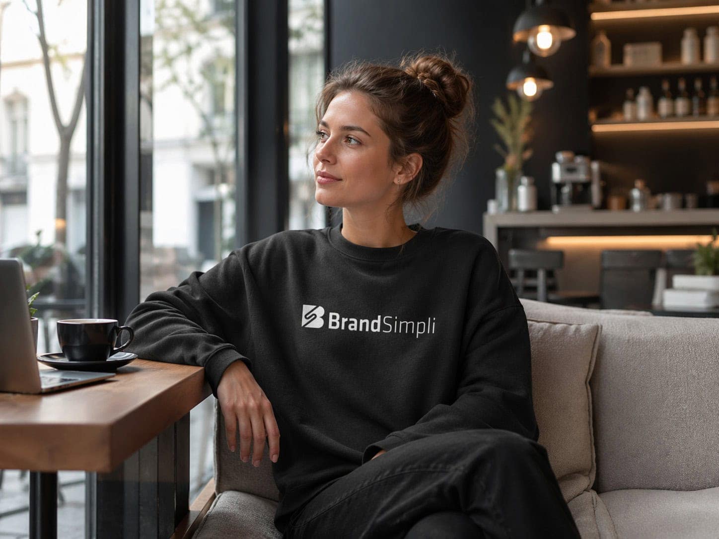 Frau trägt schwarzes Sweatshirt mit BrandSimpli Logo in modernem Café.